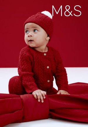 Rode trui en bijpassende muts met een pompon, beide met een getextureerd breipatroon. Kind zit op een rode stoffen achtergrond.