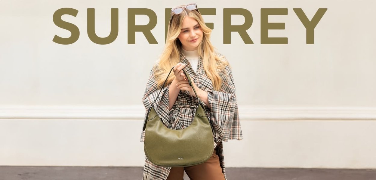 Olive green hobo bag with a pebbled texture and black accents, held by a person in a patterned scarf against a neutral background.