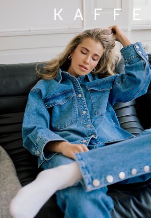 Junge Frau in Jeansjacke und Jeans sitzt mit geschlossenen Augen auf einem schwarzen Ledersofa, ihre Hand fährt durch ihr blondes Haar, darüber der Text "KAFFE".