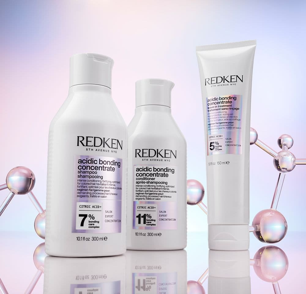 Three Redken hair care products: white bottles with black text. Shampoo contains 7% citric acid, conditioner 11%, treatment 5%.