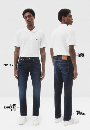 Pantalones vaqueros de mezclilla azul oscuro con pierna ajustada y cónica, talle bajo, cierre de cremallera y longitud completa. Incluyen parche trasero con marca y costuras en contraste.