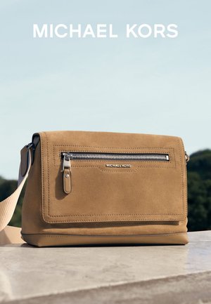 Tan mockasintvärk väskan med en framficka med dragkedja, justerbar axelrem och silverfärgad hårdvara. Har "Michael Kors"-logotyp.