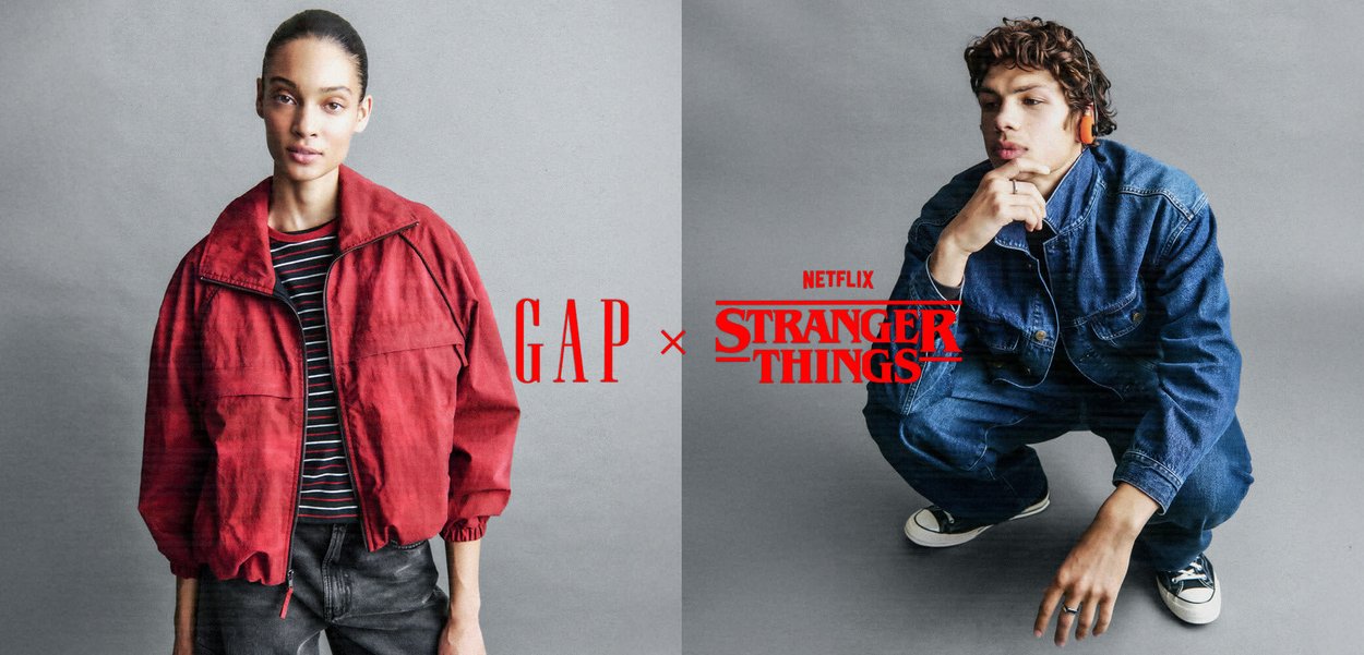 Donna con giacca rossa e pantaloni neri larghi in piedi contro uno sfondo grigio, con i loghi rossi GAP x Stranger Things Netflix sovrapposti.