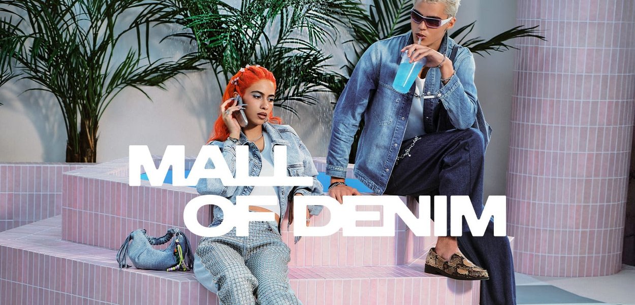 Deux mannequins sont assis sur des marches en carreaux roses. L'un porte une veste en jean bleu clair et un pantalon en jean foncé ; l'autre a un haut blanc et un pantalon à damier.
