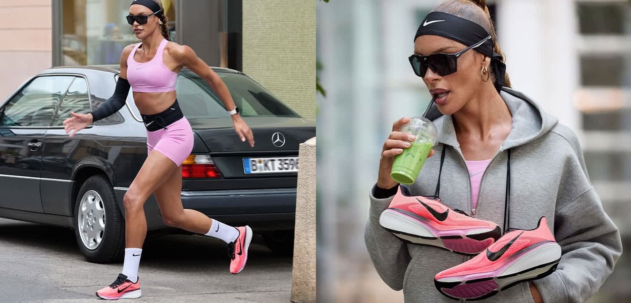 Mujer con ropa deportiva rosa corriendo junto a un coche negro, sosteniendo zapatillas Nike rosas y bebiendo un batido verde con una sudadera gris con capucha.