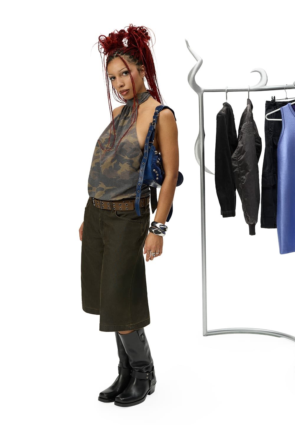 Camouflage haltertop, olijfgroene cropped broek, zwarte kniehoge laarzen, zilveren riem met ogen, blauwe handtas, moderne hanging rack.