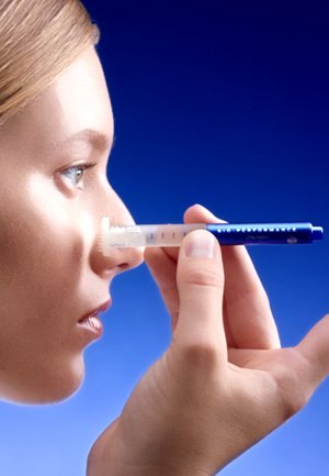 Medical syringe with a clear barrel, blue accents, and a white tip, held near a person's nose against a gradient blue background.