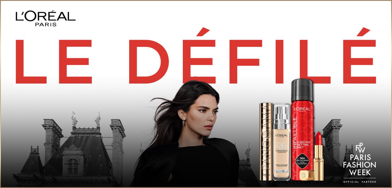 Produkty L'Oréal Paris, w tym złota podkład, mgiełka do utrwalania w kolorze czerwonym oraz czerwona pomadka, wyeksponowane na tle czarno-białego paryskiego krajobrazu.
