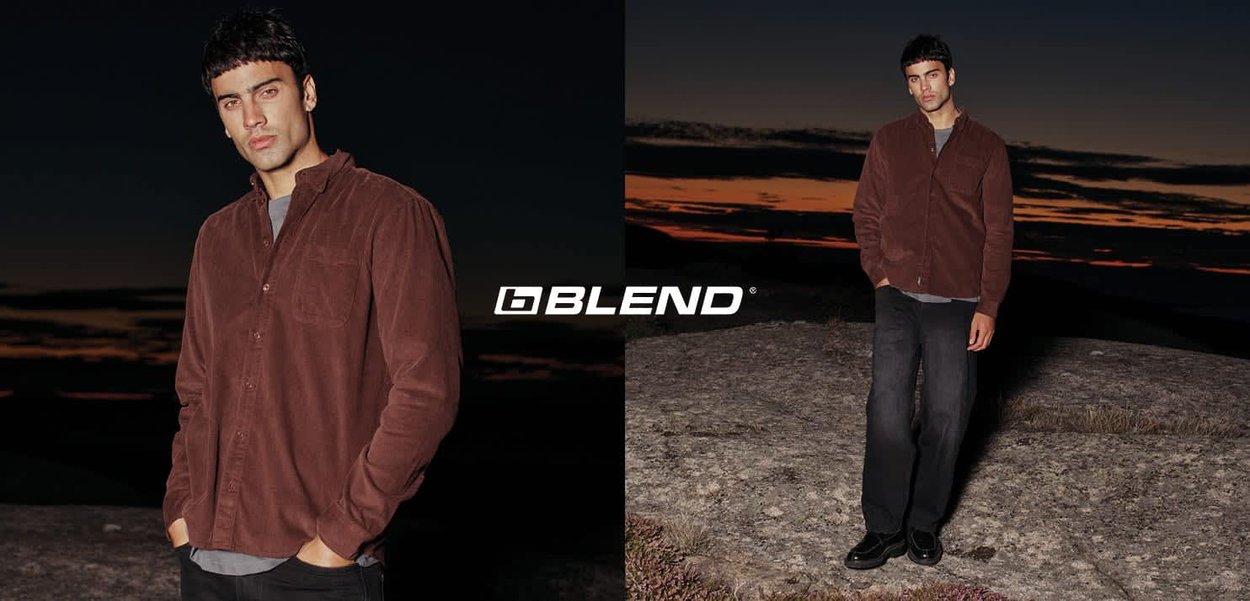 Bruin ribfluwelen overhemd met een button-down kraag, gecombineerd met donkerblauwe spijkerbroek en zwarte schoenen, tegen een achtergrond van een zonsondergang.