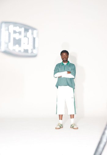 Groen kraag polo shirt over een witte lange mouwen shirt, gecombineerd met witte cropped pants met groene strepen en een paarse sneakers.