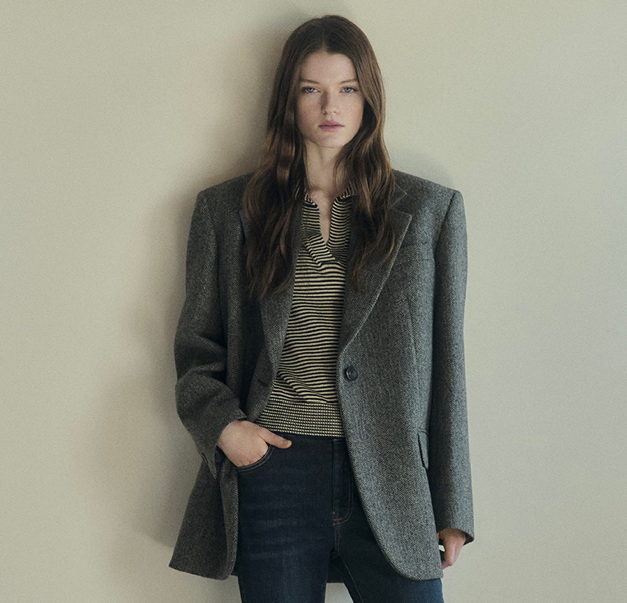 Gray oversized blazer with a textured wool fabric, single button closure, and notched lapels, worn over a striped shirt and jeans.