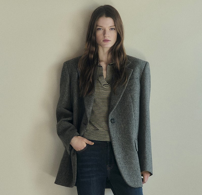 Gray oversized blazer with a textured wool fabric, single button closure, and notched lapels, worn over a striped shirt and jeans.