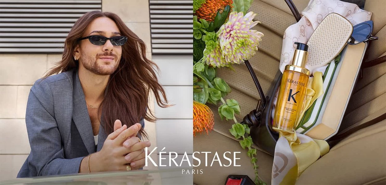 Kérastase-Haaröl in einer klaren Flasche mit goldenen Akzenten, daneben eine gemusterte Haarbürste, Sonnenbrille und bunte künstliche Blumen auf einer beigen Oberfläche.