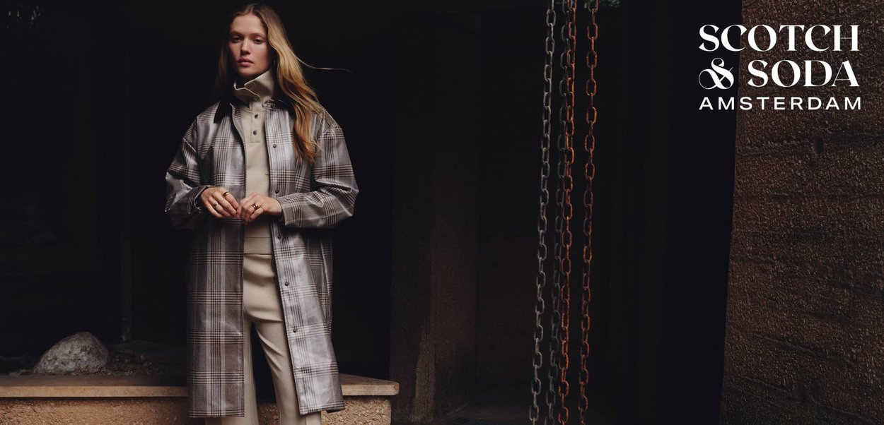 Manteau à carreaux dans des tons beige et gris, avec une fermeture à boutons, porté sur un pull crème. Fond texturé avec des chaînes.