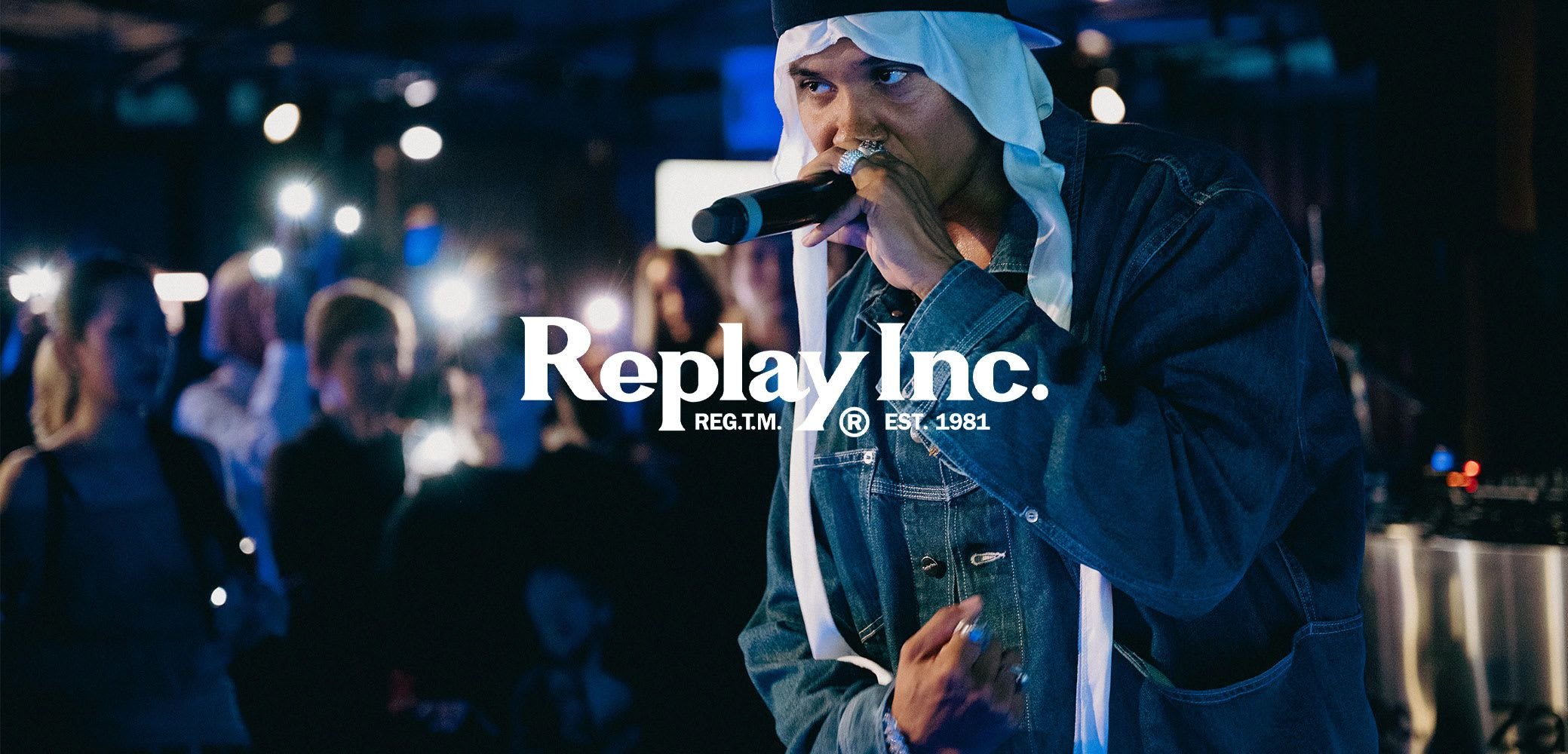 Rapper in Jeansjacke und weißem Kopftuch, der mit Mikrofon in der Hand performt, während die Menge im Hintergrund ihre leuchtenden Handys hochhält.