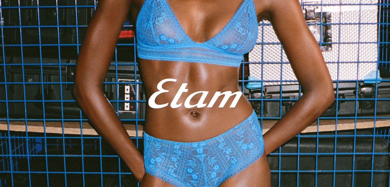 Blauwe kanten bralette en bijpassende hipster onderbroek met bloemenpatronen. Model poseert tegen een blauwe draadrooster achtergrund. Merkennaam "Etam" weergegeven.