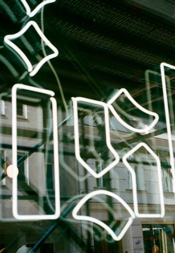 Neonreclame met geometrische vormen die op een reflecterend oppervlak worden weergegeven, met witte lijnen in verschillende vormen, tegen een gebouwachtergrond.