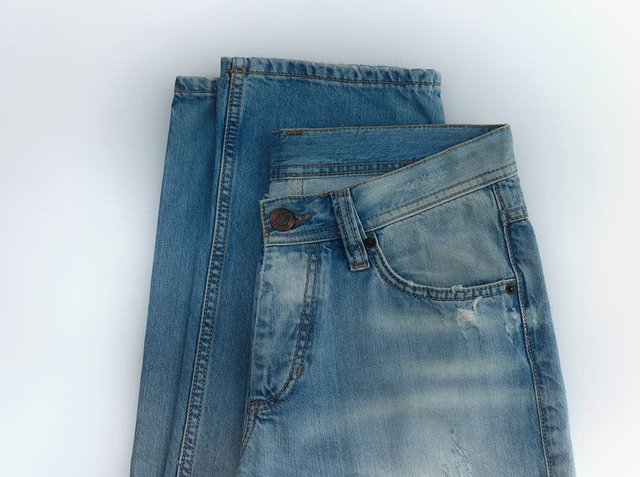 Denim jeans stacked, featuring a light blue color, distressed texture, classic five-pocket design, and a metal button on the waistband.
