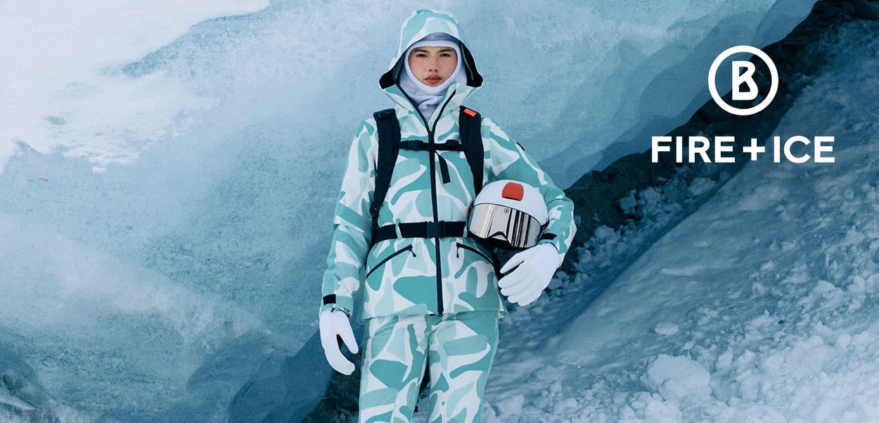 Jasnoniebieski i biały kombinezon narciarski w kamuflażu z kapturem, czarnymi akcentami i paskami. Model trzyma biały kask z lustrzaną szybą.