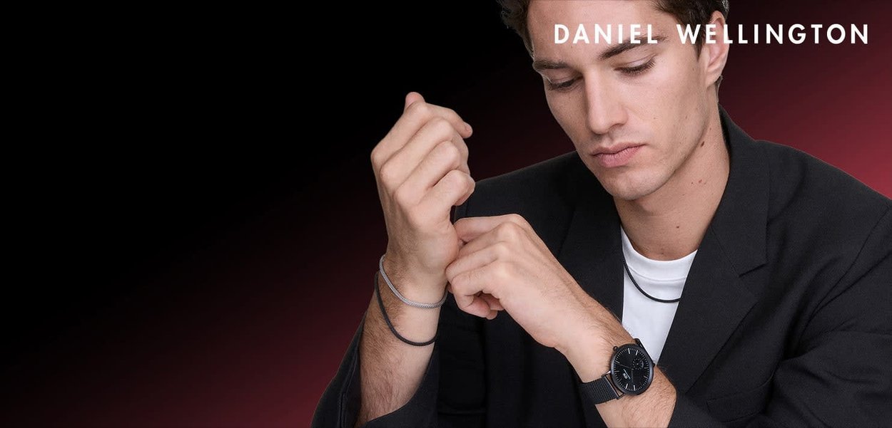 Orologio analogico nero con quadrante rotondo e cinturino testurizzato. Il modello indossa un blazer nero sopra una camicia bianca, mostrando uno stile minimalista.