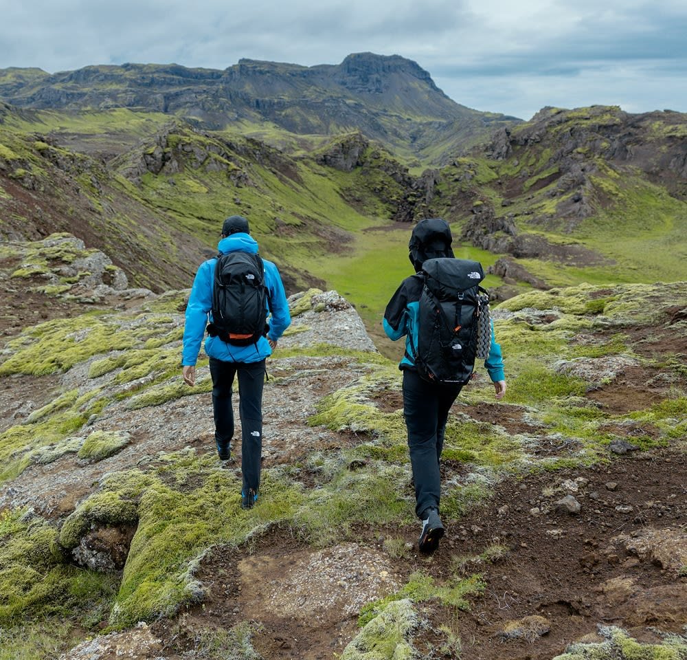 Due hikers attraversano un paesaggio roccioso, uno con una giacca blu e l'altro in nero. Entrambi portano zaini neri, con trame diverse.