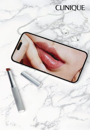 Smartphone met close-up van lippen, zilveren lipsticktube, cilindrische zilveren verpakking en zilveren oorringen op een marmeren achtergrond.
