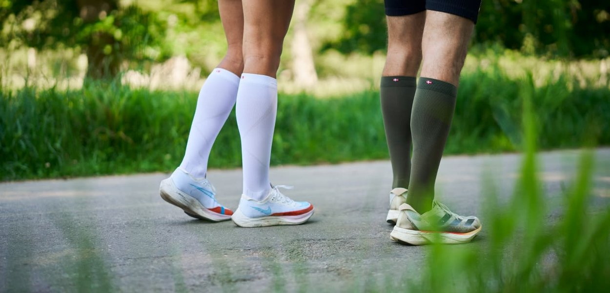 Deux personnes marchant en plein air sur un chemin pavé, portant des chaussettes de compression et des chaussures de sport, entourées de verdure.