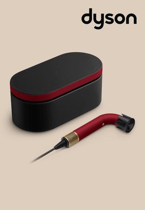 Sort og rød elektronisk enhed designet af Dyson med et buet håndtag og sort opbevaringsetui på beige baggrund.