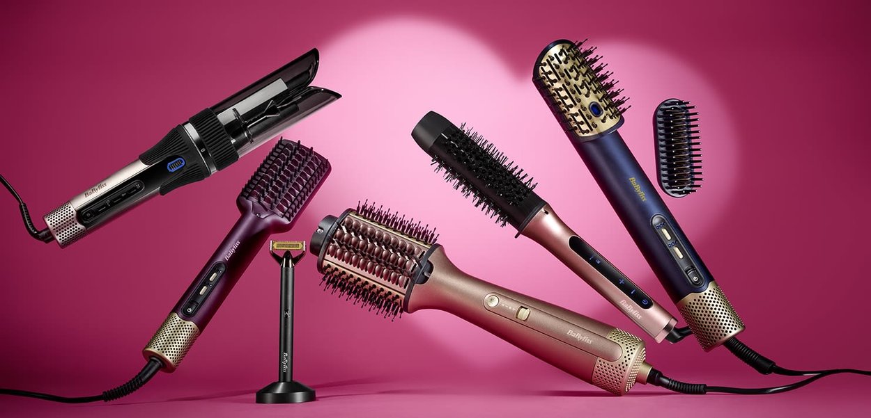 Fem elektriske hårstylingsbørster og en skjeggtrimmer for ansiktet står på en rosa bakgrunn med ledninger synlige.