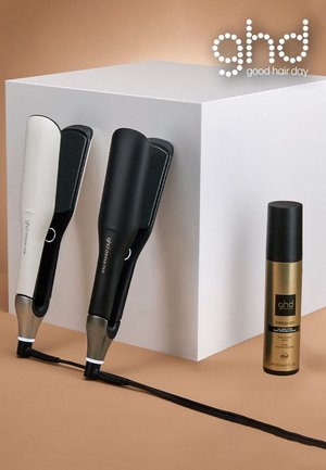 Lisseurs GHD en noir et blanc, avec des poignées lisses et des plaques rembourrées, accompagnés d'un vaporisateur doré pour la protection contre la chaleur.