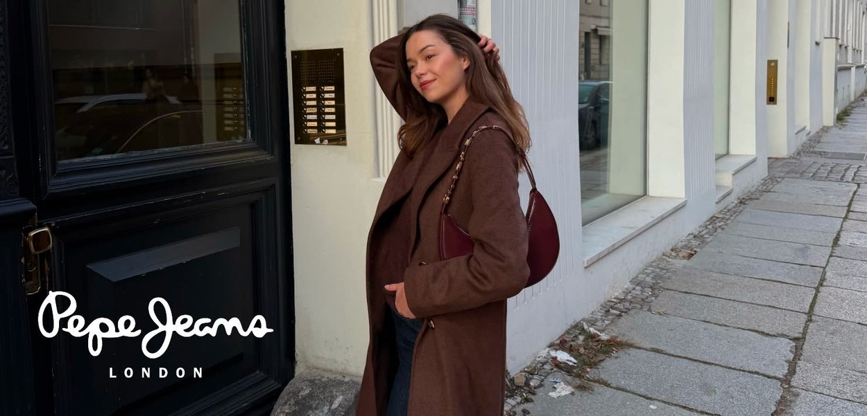 Abrigo de lana marrón con diseño en capas, con cuello tipo chal. Un pequeño bolso burdeos colgado sobre el hombro. Entorno urbano.