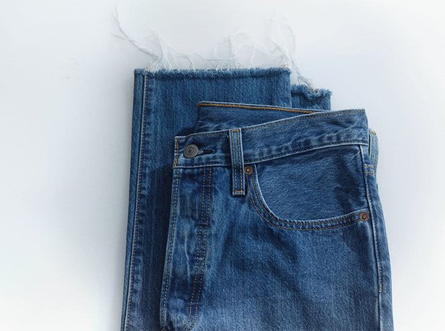 Denim jeans in dark blue with a frayed hem. They feature a classic five-pocket design, button closure, and contrasting stitching details.