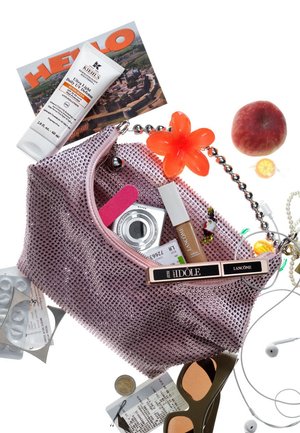 Pink mesh handbag with a bejeweled finish; contains cosmetics, a camera, a flower accessory, an apple, and various small items.