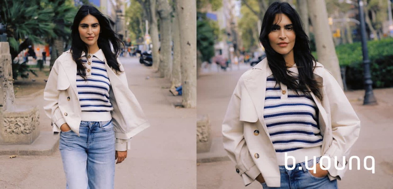 Frau trägt einen gestreiften Pullover, eine leichte Jacke und Jeans, geht auf einem von Bäumen gesäumten städtischen Weg mit den Händen in den Taschen.