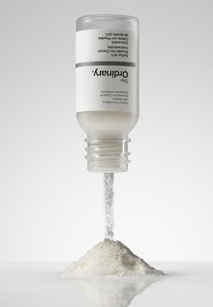 Bouteille de poudre de squalane de The Ordinary versant une fine poudre blanche sur une surface blanche lisse.