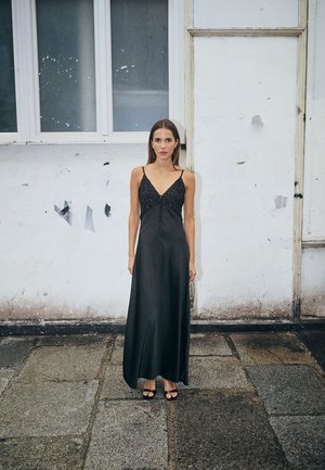 Black satin evening gown with a V-neck, embellished neckline, and thin straps. Smooth texture and long, flowing silhouette.