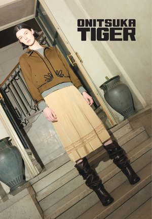 Bruine geborduurde jas, grijze trui, roomkleurige rok met kanten rand, en kniehoge bruine leren laarzen. Elegant, zachte texturen, modern design.