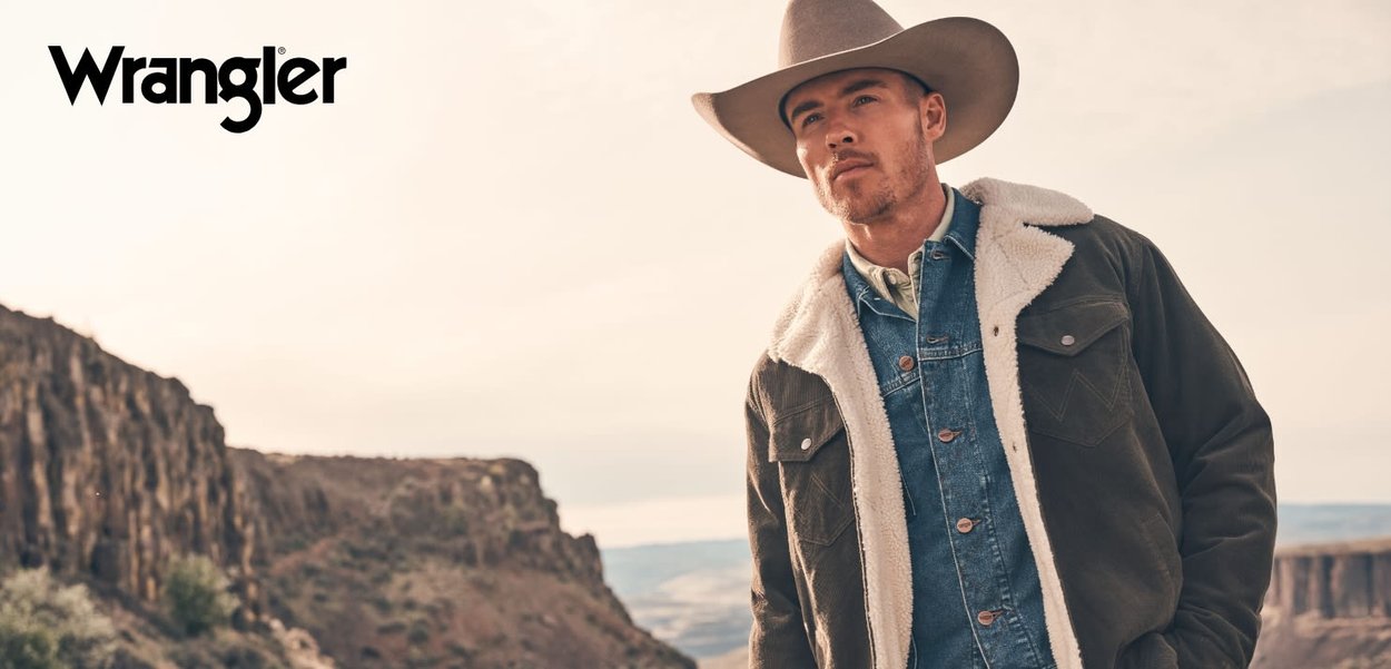Wrangler jacket with a dark green fabric, shearling collar, and denim shirt underneath. A wide-brimmed hat completes the outfit.