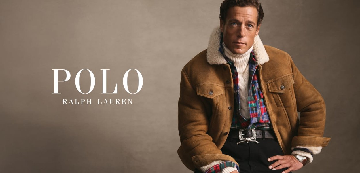 Braune Wildlederjacke mit Schalenzottelkragen, kombiniert mit einem karierten Hemd, einem weißen Rollkragenpullover und schwarzen Hosen, ergänzt durch eine metallische Gürtelschnalle.