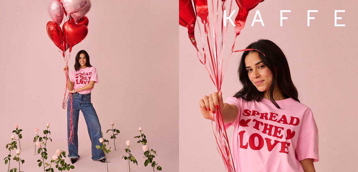 Junge Frau in einem rosa "Spread the Love"-Shirt hält rote und rosa herzförmige Luftballons vor einem rosa Hintergrund mit Rosen darunter.