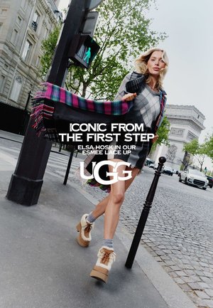 Woman walking on city street near Arc de Triomphe wearing patterned dress, colorful scarf, and tan fur-lined lace-up boots.