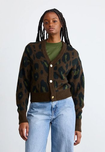 Bruine luipaardprint cardigan met groene accenten, knoopsluiting, geribbelde manchetten en zoom, gedragen over een groene top, gecombineerd met lichtblauwe jeans.