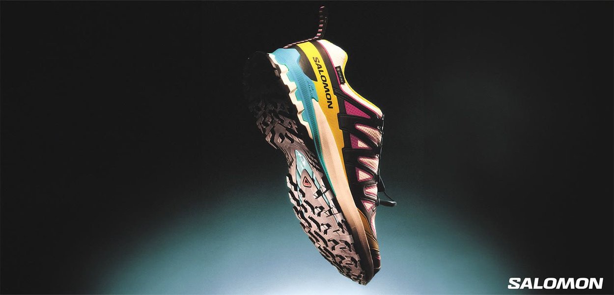 Scarpa da trail running con tomaia multicolore che presenta tonalità di blu, rosa e giallo, suola nera texturizzata e logo del marchio prominente.