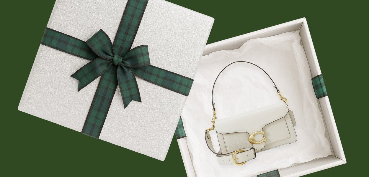 Borsa firmata bianca con dettagli in oro all'interno di una scatola regalo bianca con nastro a quadri verde scuro su sfondo verde scuro.