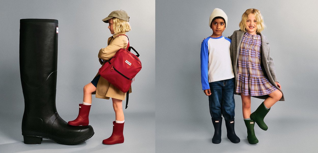 Zwei Kinder tragen bunte Gummistiefel; eines steht neben einem übergroßen schwarzen Stiefel, das andere posiert mit einem Freund vor einem grauen Hintergrund.