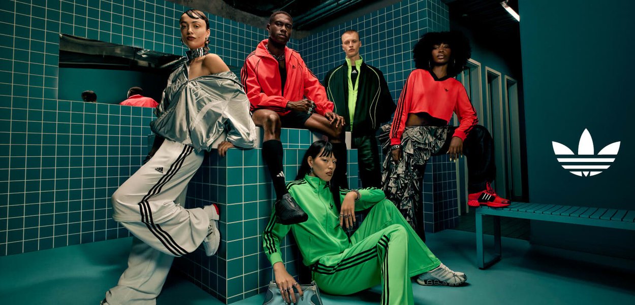 En grupp på fem personer i sportiga kläder. Kläderna har starka färger, mönster och texturer. Bakgrunden har teal-färgade plattor; Adidas-logotypen syns.