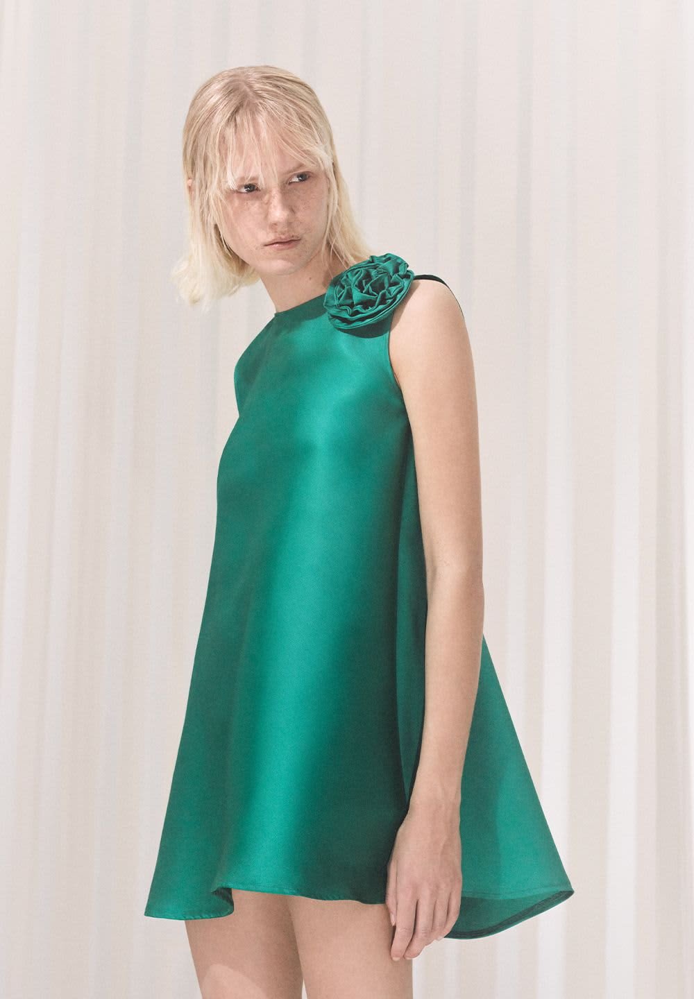 Green satin dress with a smooth texture, featuring a flower accent on the shoulder. A-line shape, sleeveless design, knee-length hem.