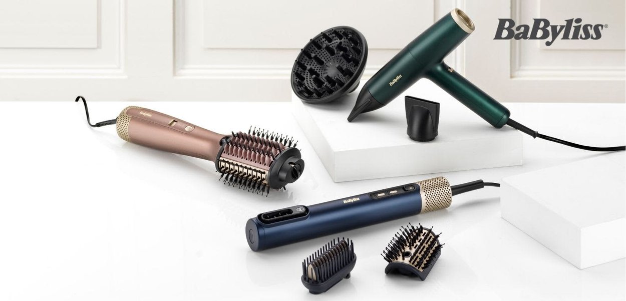 Hårstylingværktøjer inklusive en rundbørste i rosenguld, en blå opvarmet børste, en grøn hårtørrer og tilbehør på hvide overflader.