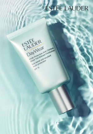 Estee Lauder DayWear, a light turquoise tube with a silver cap, features black and gold text, set against a reflective water background.