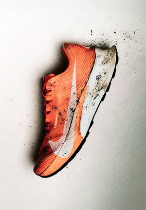 Scarpa da corsa arancione brillante con logo swoosh bianco, suola bianca sporca e schizzi di fango su uno sfondo chiaro.